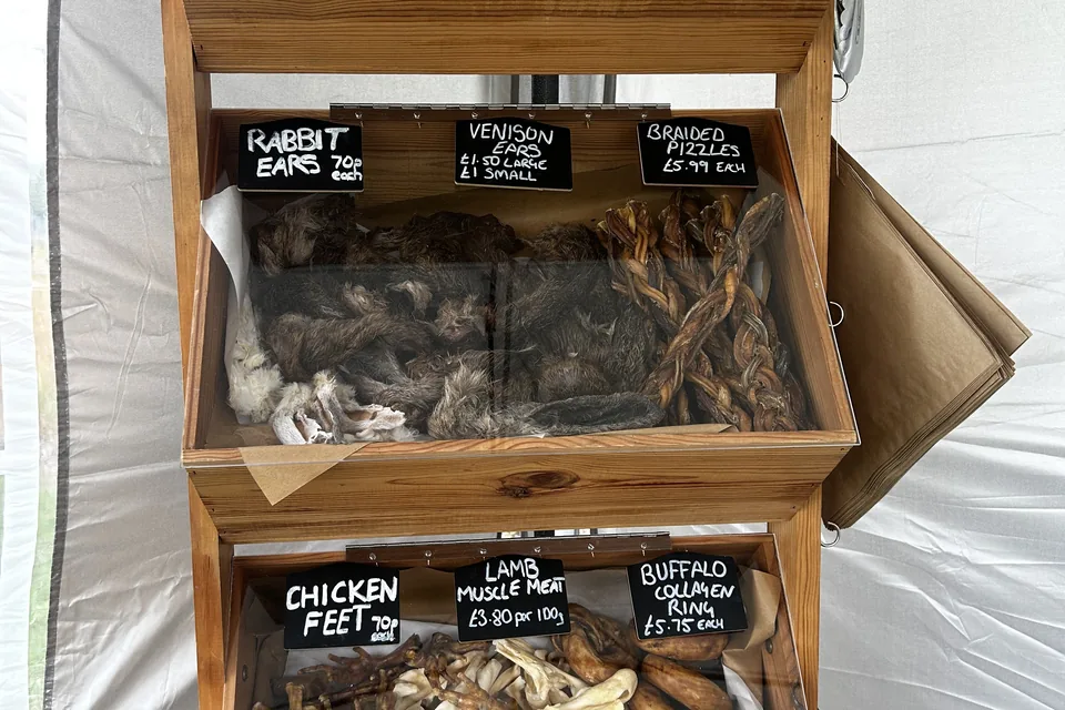 Wooden crates of natural chews with chalked labels: rabbit ears, venison ears, chicken feet