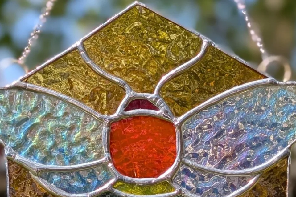 A stained-glass bee suncatcher in amber, red and iridescent glass, hanging in sunlight